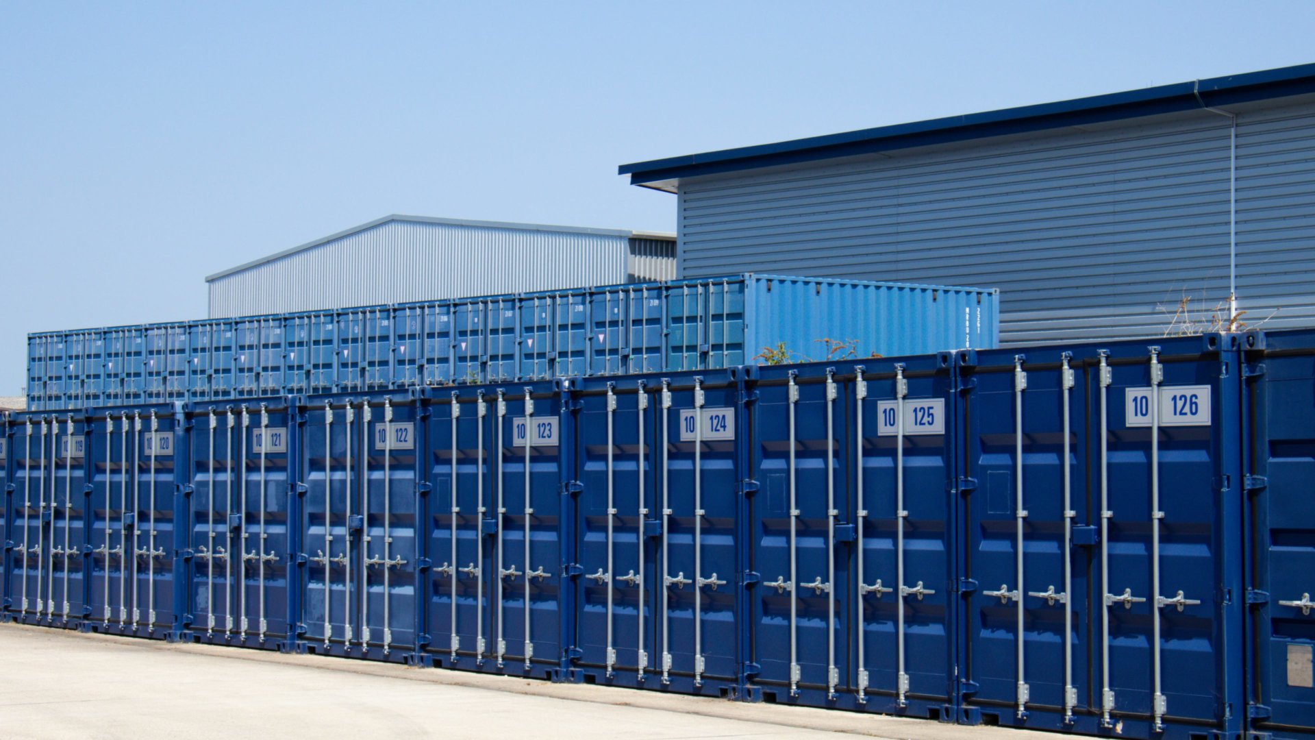A long row of eight blue self storage containers with metal bars.